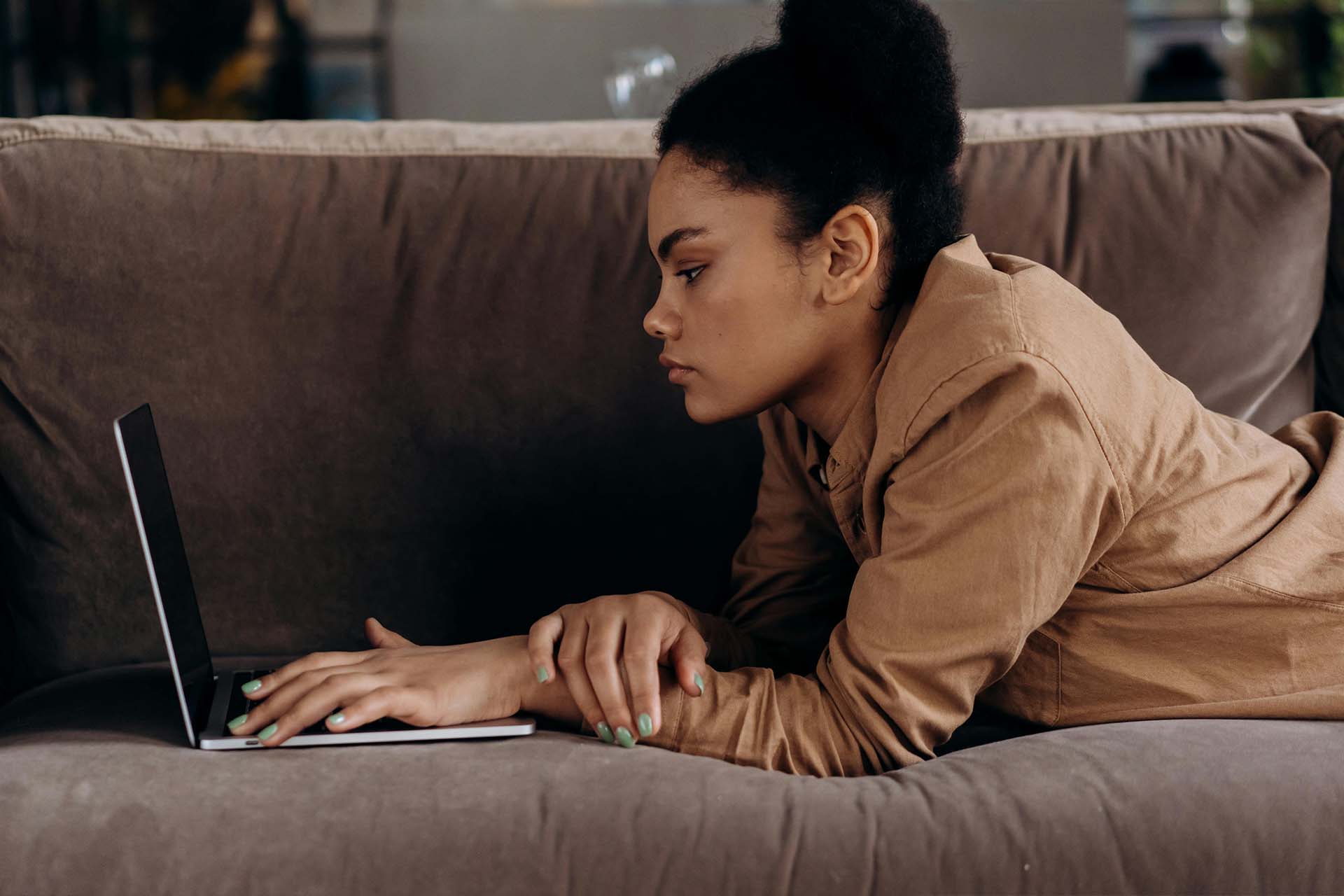 en kvinna ligger i soffa och använder en laptop