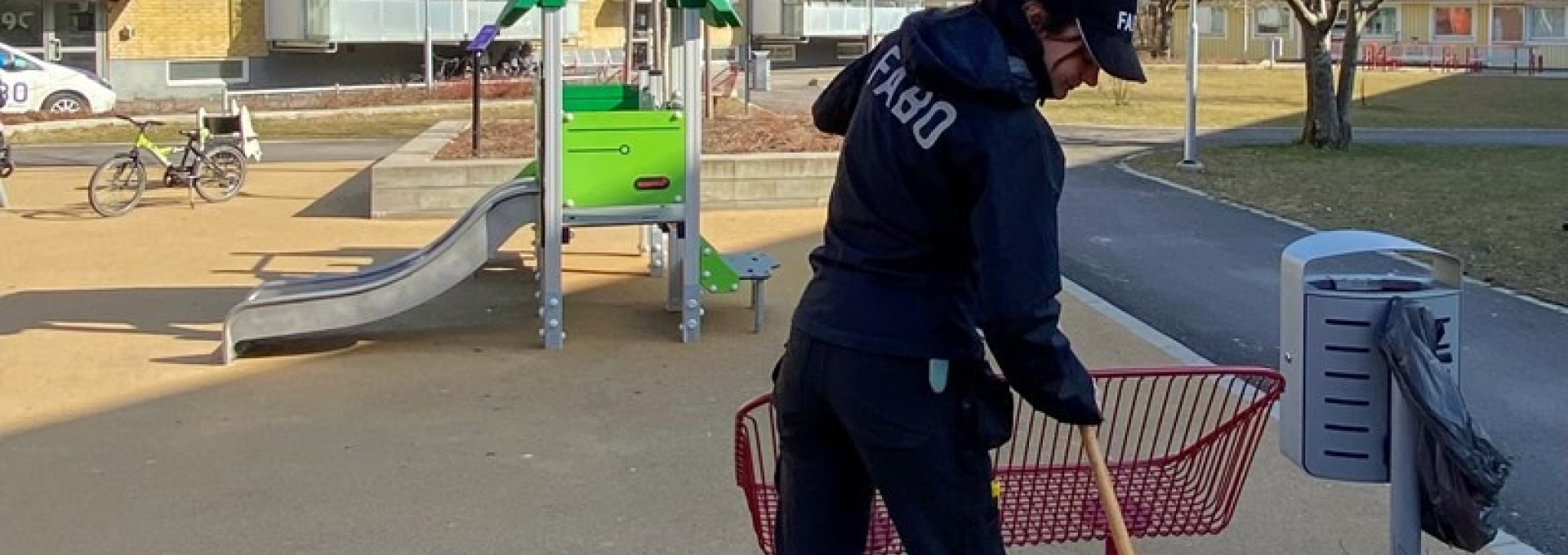 Kvinna i Fabokläder räfsar i en rabatt bredvid en lekplats.