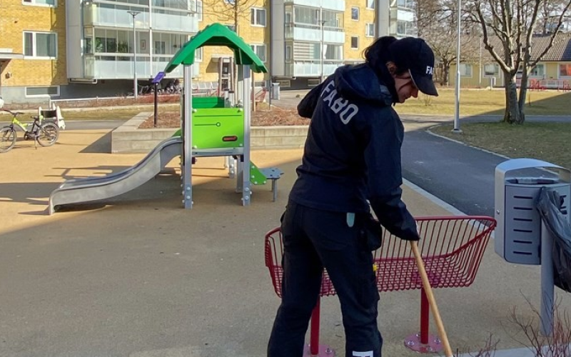 Kvinna i Fabokläder räfsar i en rabatt bredvid en lekplats.
