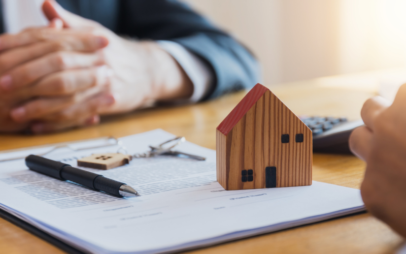 Två personers händer med ett papper emellan sig, med nyckel, penna och en husfigur